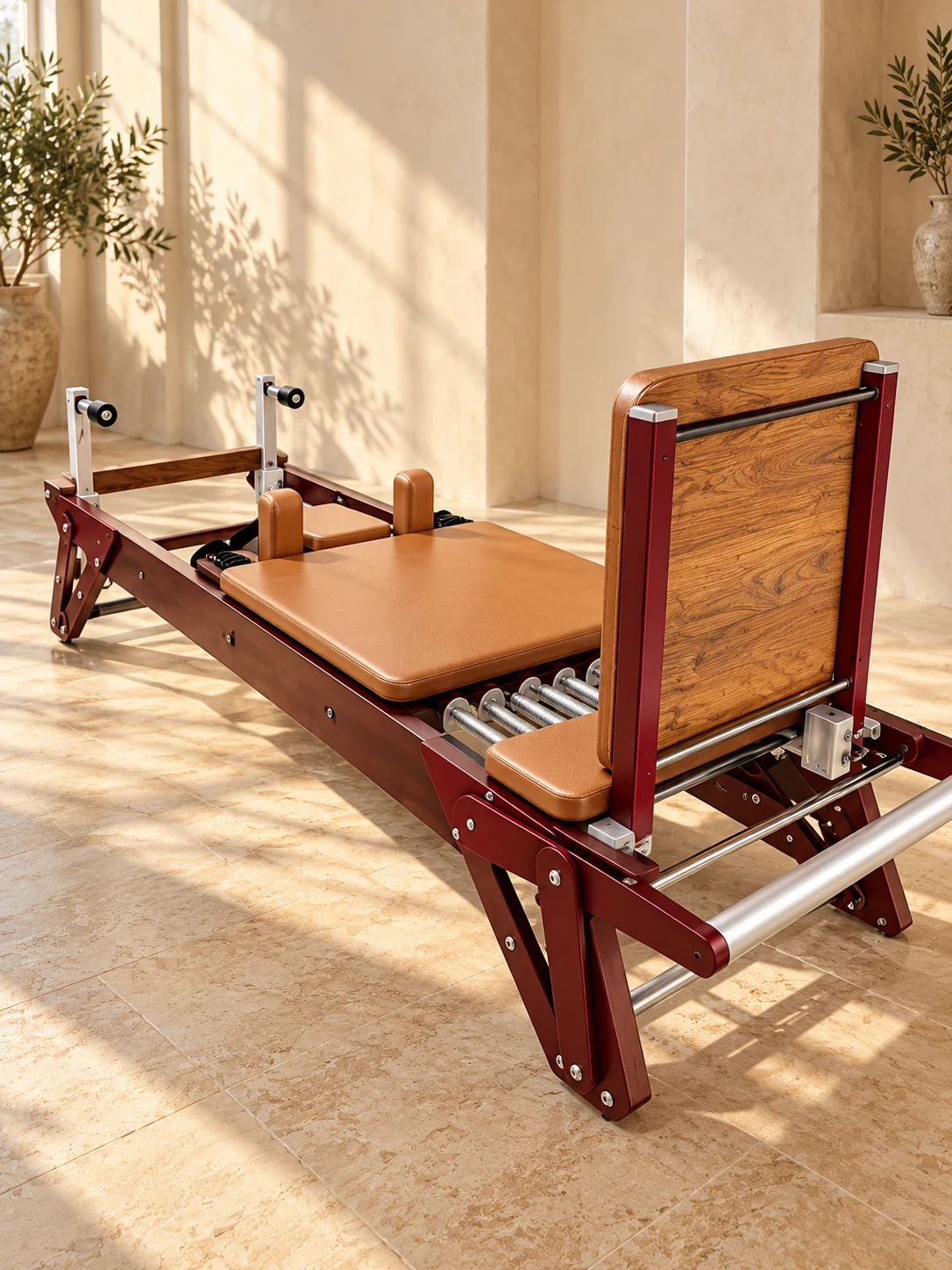 Reformer de Pilates con estructura burdeos, tapizado caramelo, rieles plateados y respaldo de madera.